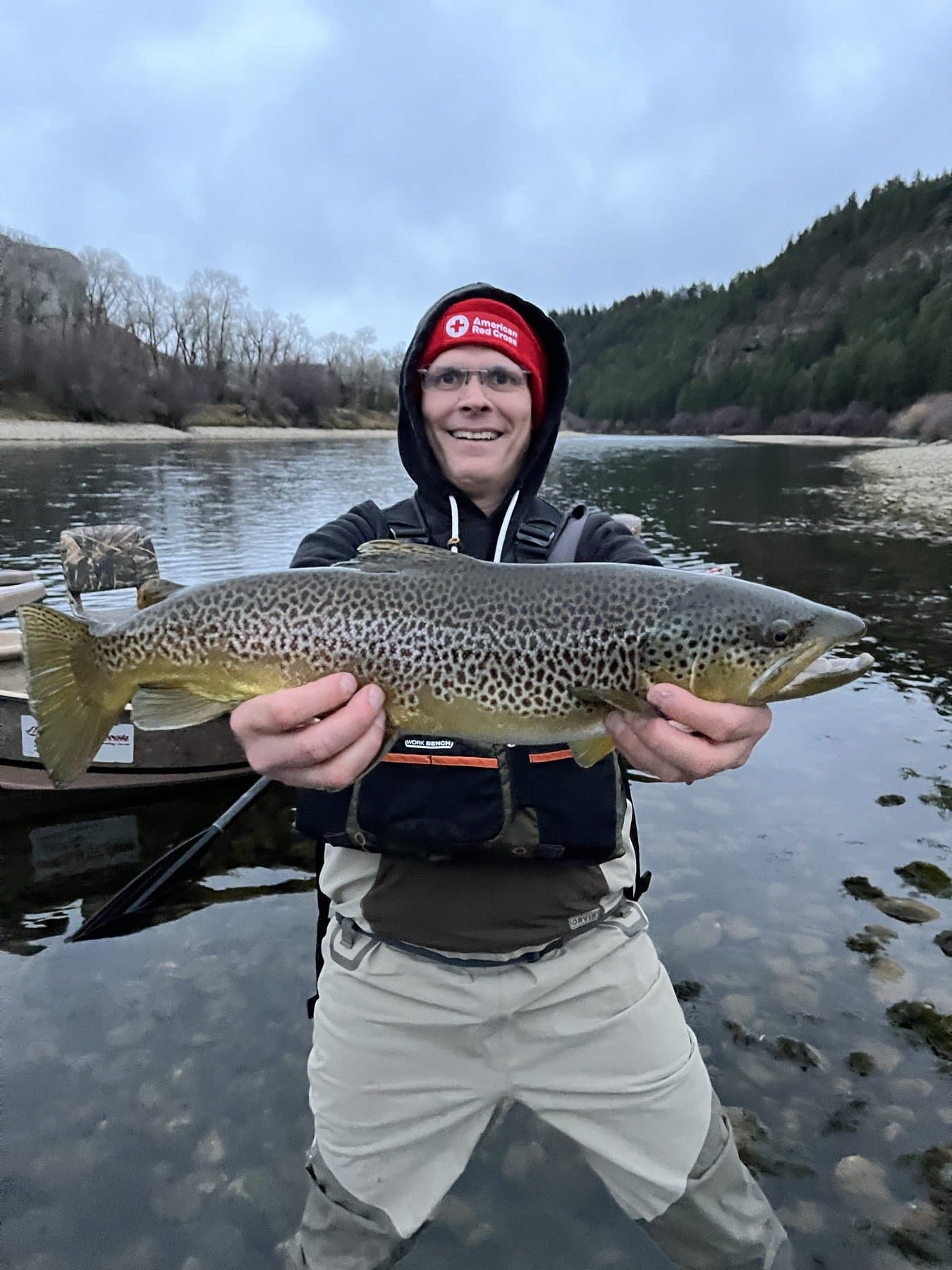 Angler holding a large South Fork brown trout beside a drift boat