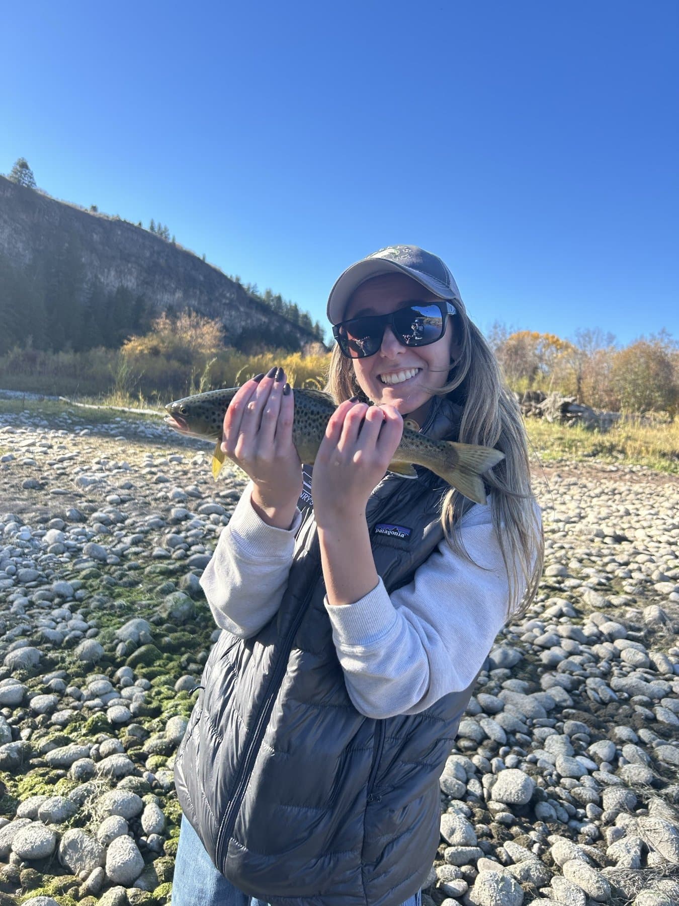 Angler holding a brown trout on a gravel bar