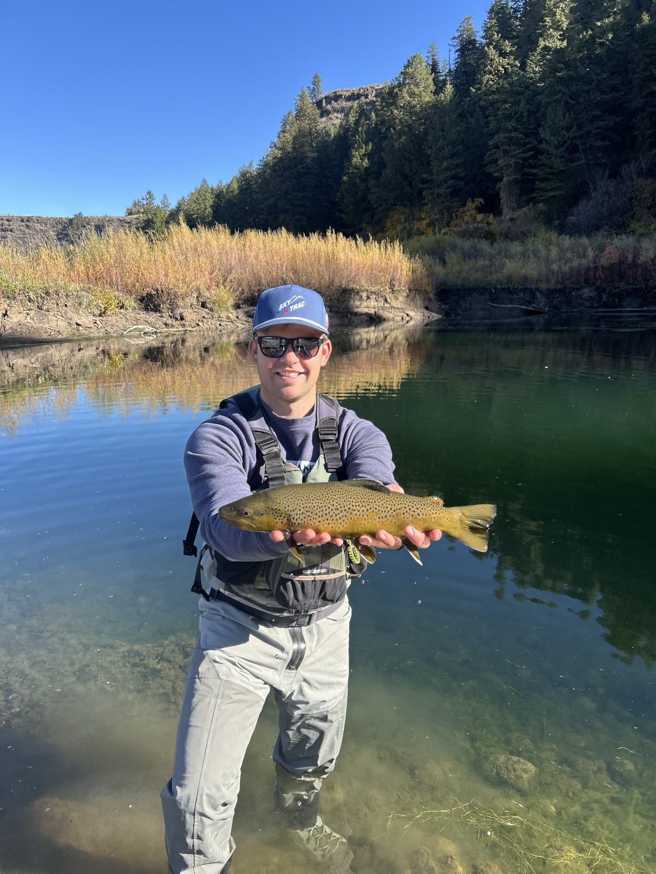 Angler holding a brown trout beside a calm pool